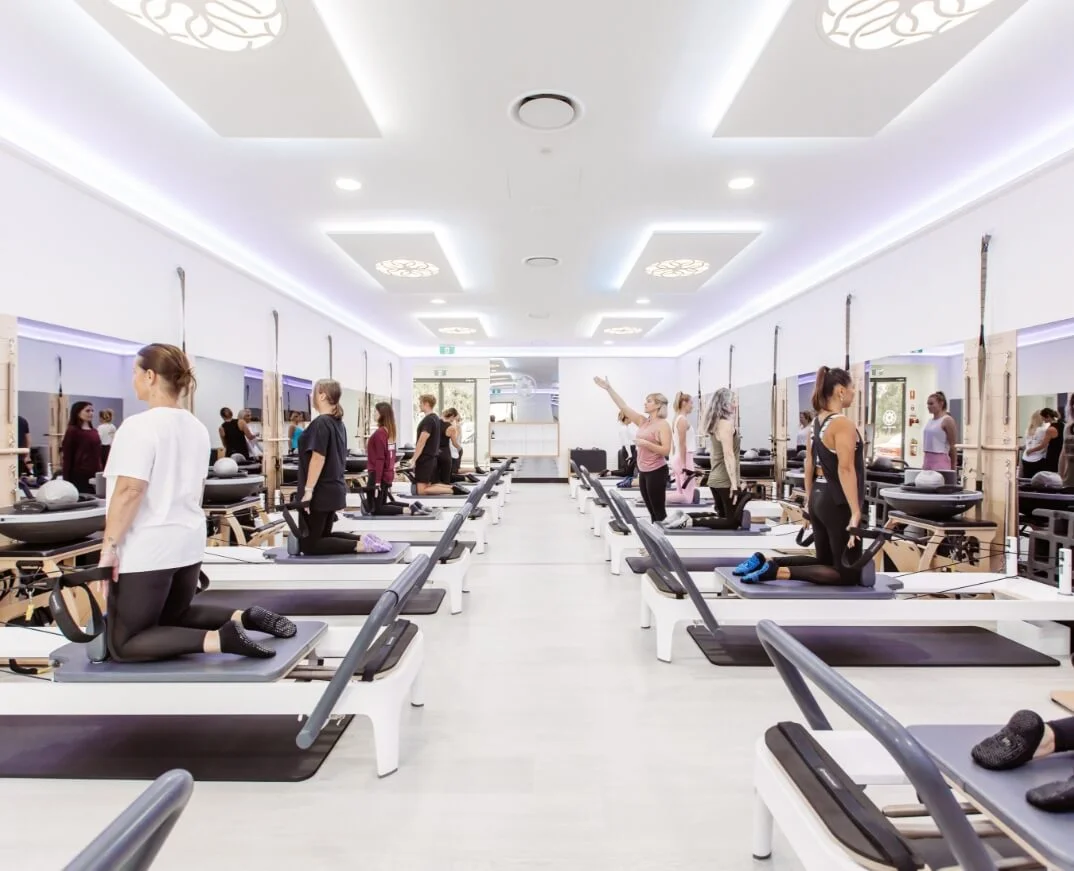 A pilates class in a gym with many people doing pilates.