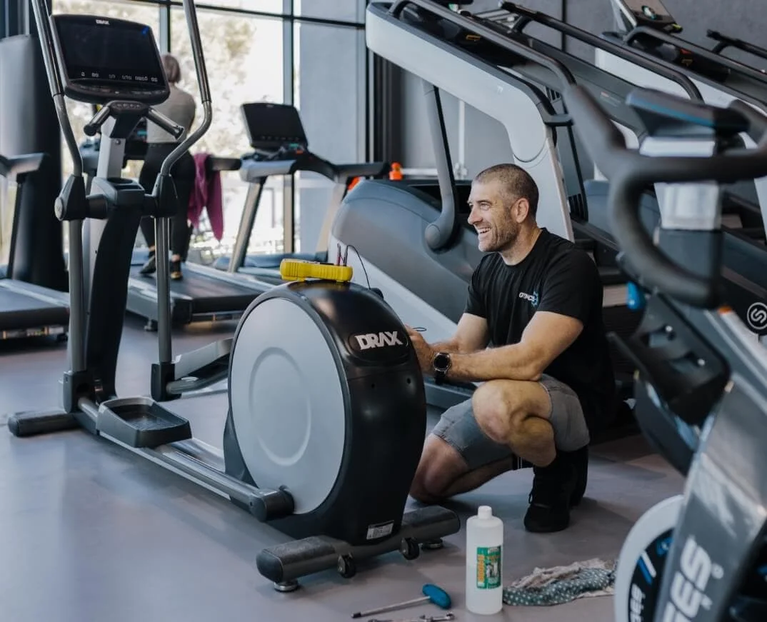 A man kneeling on an exercise bike in a gym.