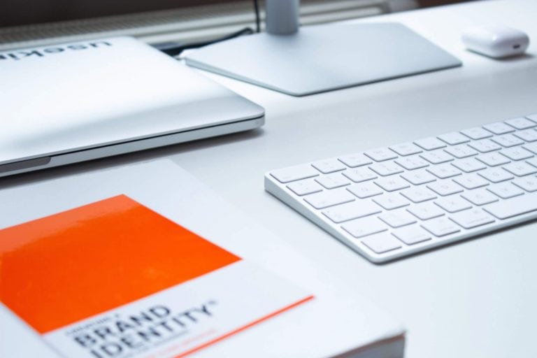 A white desk with an orange book, keyboard and mouse.