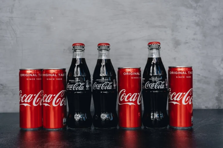 Five cans of coca cola with branding sitting on a table.